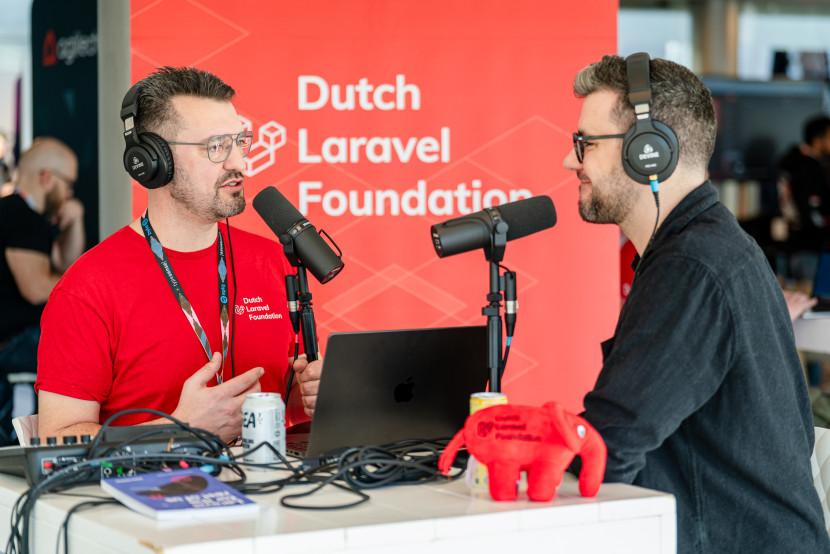 Two men are engaged in a conversation at a podcast setup. One wears a red t-shirt with 