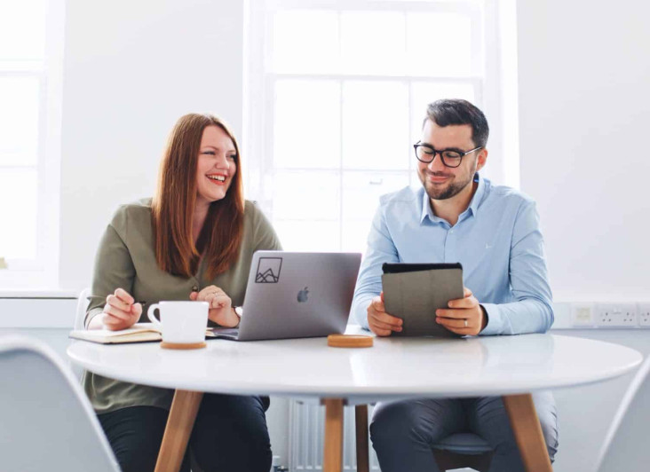 Two people looking at a laptop screen and a tablet