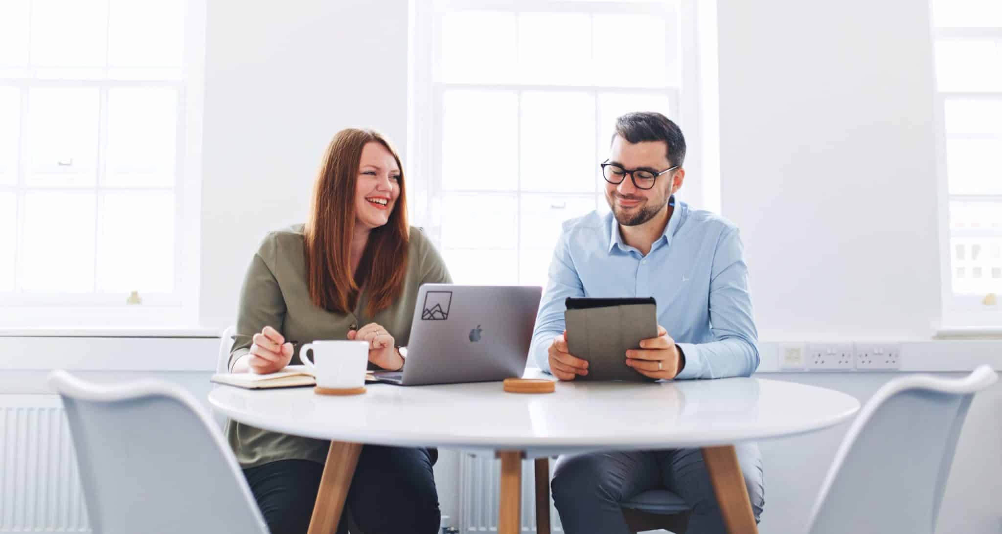 Two people looking at a laptop screen and a tablet