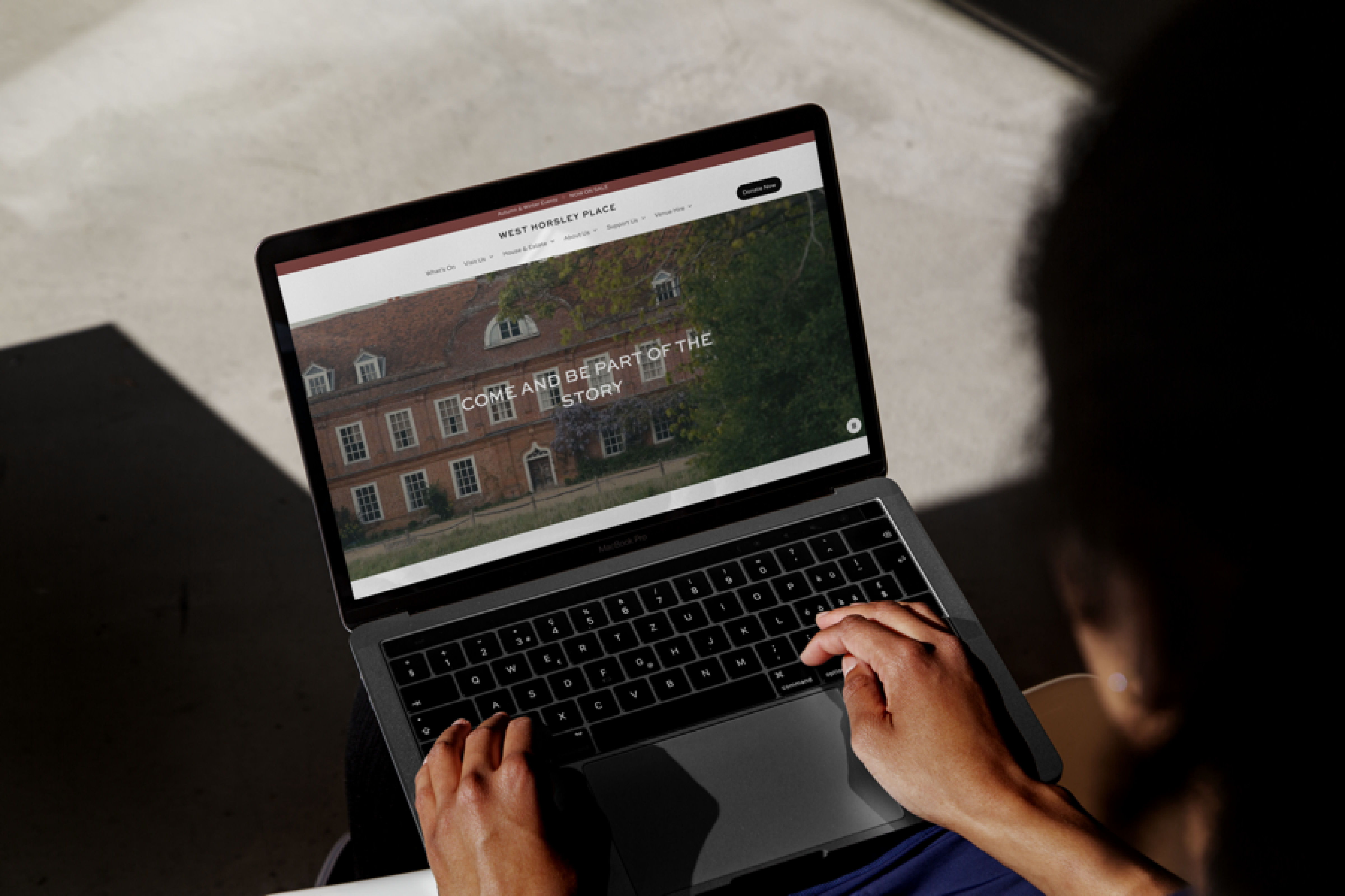 A person using a laptop to view a website featuring a historic building, with text inviting users to 